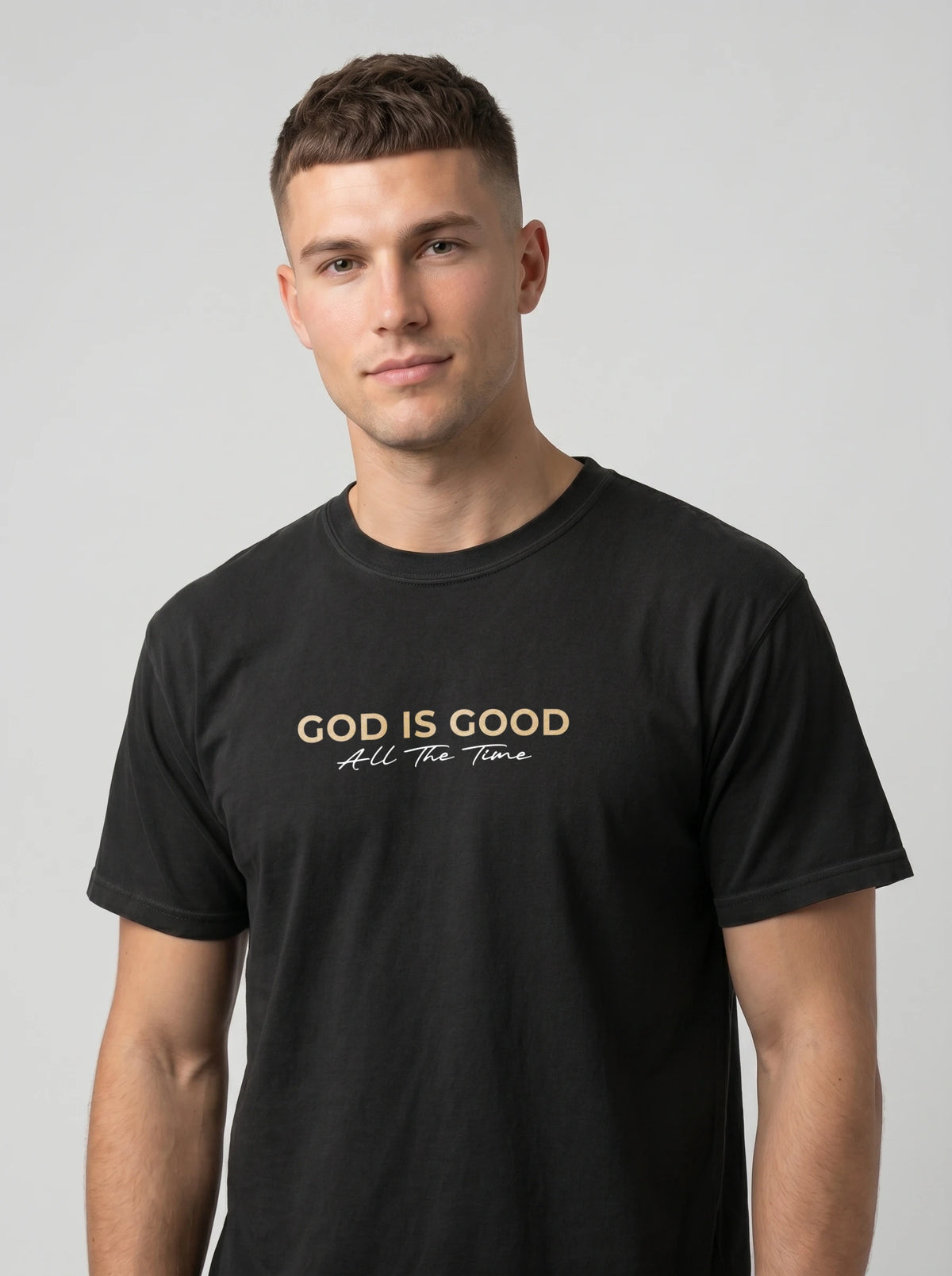Man wearing black “God Is Good All The Time” Christian graphic T-shirt with beige and white lettering.