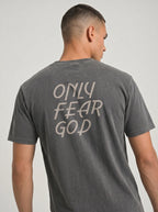 A man wearing a dark gray washed t-shirt, viewed from the back. The shirt features the phrase 'ONLY FEAR GOD' printed in a light beige hand-drawn font across the upper back.