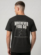 A man viewed from the back wearing a black t-shirt with a large white graphic print on the back that reads 'WHEREVER YOU GO' and 'FOR THE LORD YOUR GOD IS WITH YOU'.