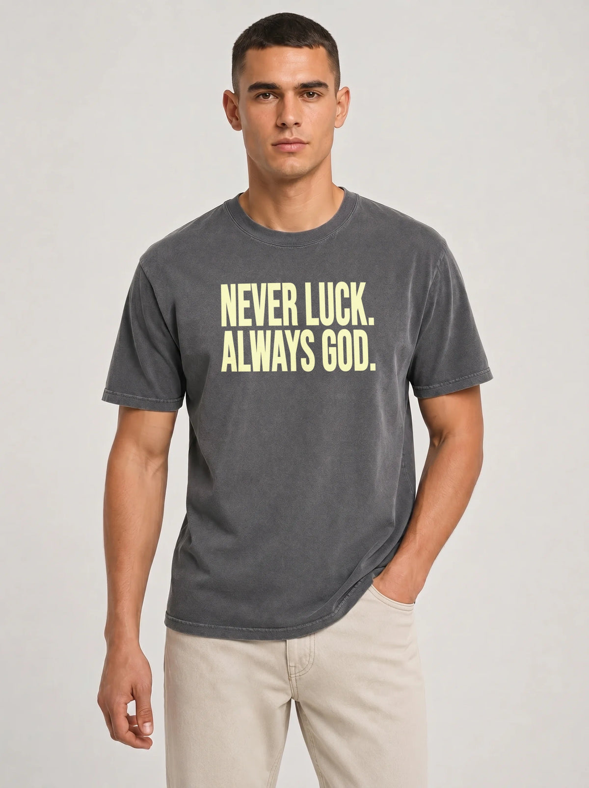 Person wearing a faded charcoal T-shirt reading “Never luck. Always God.” in pale yellow lettering.