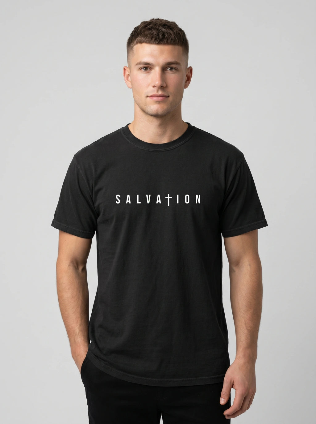 A man wearing a black crewneck t-shirt with the word 'SALVATION' printed in white across the chest, posed against a solid light gray background.