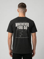 A man viewed from behind wearing a black t-shirt with a large white graphic print on the back that reads 'WHEREVER YOU GO' with a mountain and road illustration, against a light gray studio background.