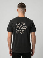 A man viewed from behind wearing a black t-shirt with the phrase 'ONLY FEAR GOD' printed in a light beige hand-drawn font on the back, set against a plain light gray background.
