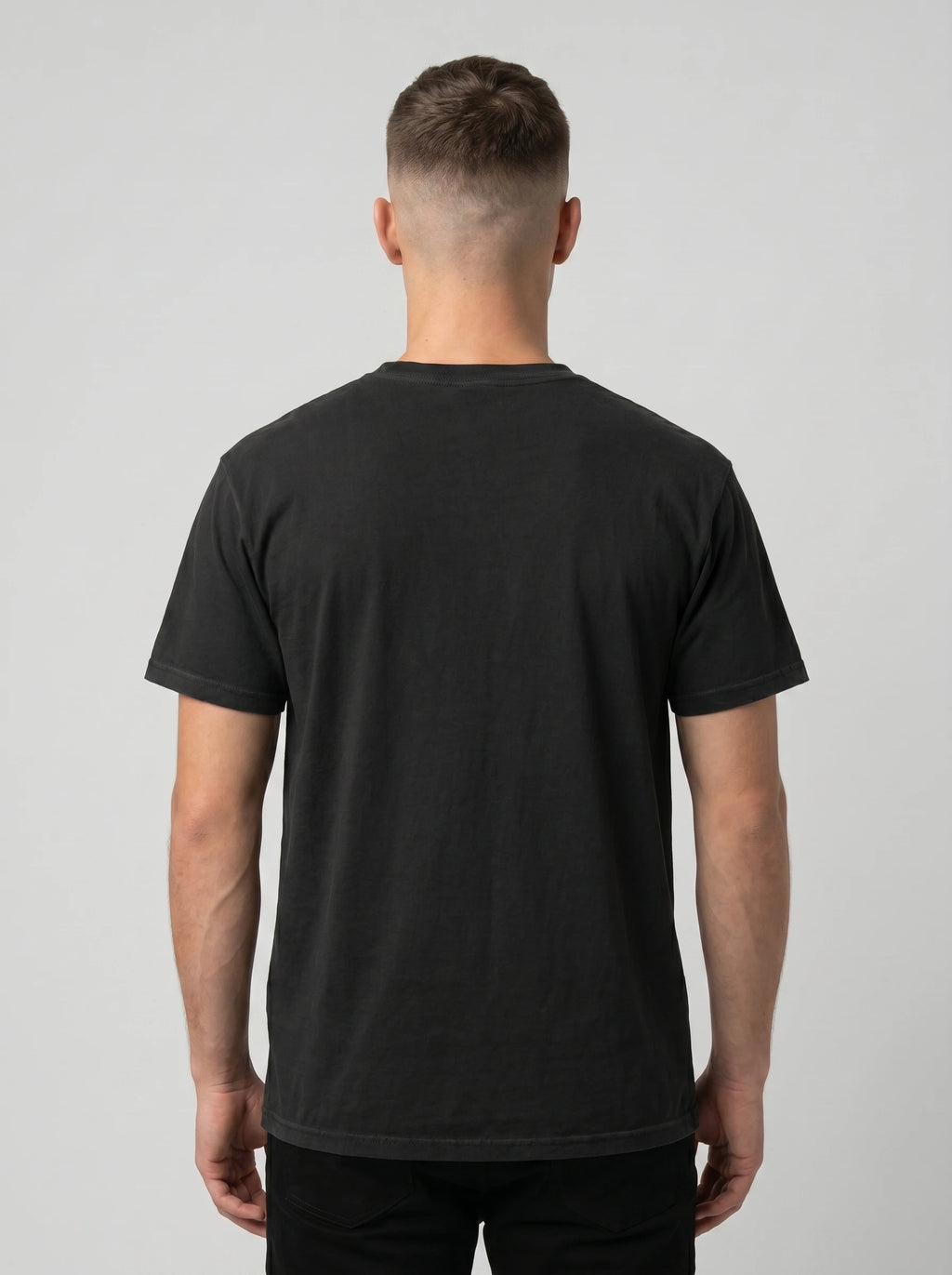 A man viewed from behind wearing a plain black short-sleeve crewneck t-shirt against a light gray studio background.
