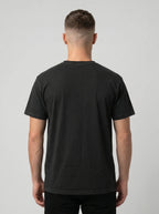 A man viewed from behind wearing a plain black short-sleeve crewneck t-shirt against a light gray studio background.