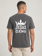 A man viewed from the back wearing a dark gray washed t-shirt with a white graphic of a crown and the text 'JESUS IS KING'.