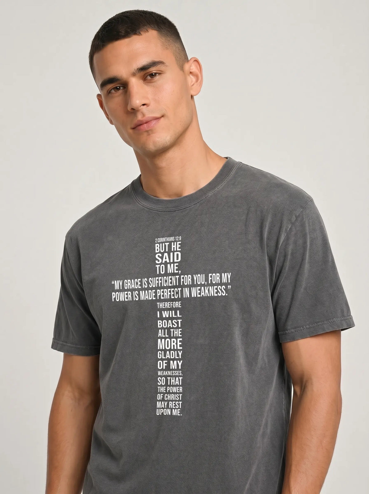 Person wearing a washed charcoal-gray T-shirt printed with 2 Corinthians 12:9, including “My grace is sufficient for you, for my power is made perfect in weakness.”