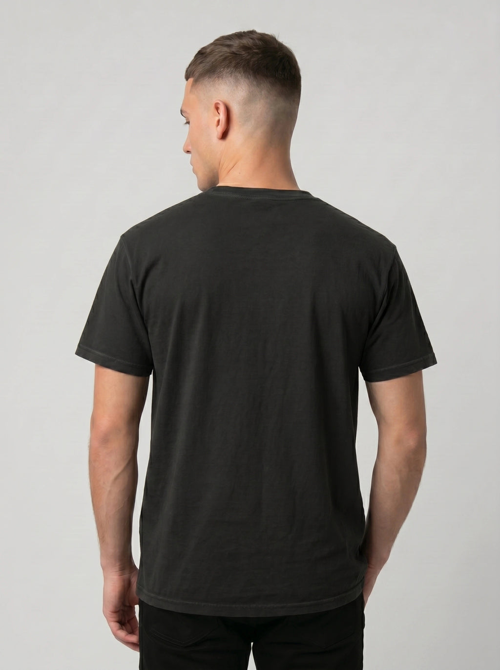 A man viewed from the back wearing a plain black short-sleeve crewneck t-shirt against a light gray studio background.