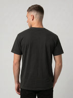 A man viewed from the back wearing a plain black short-sleeve crewneck t-shirt against a light gray studio background.