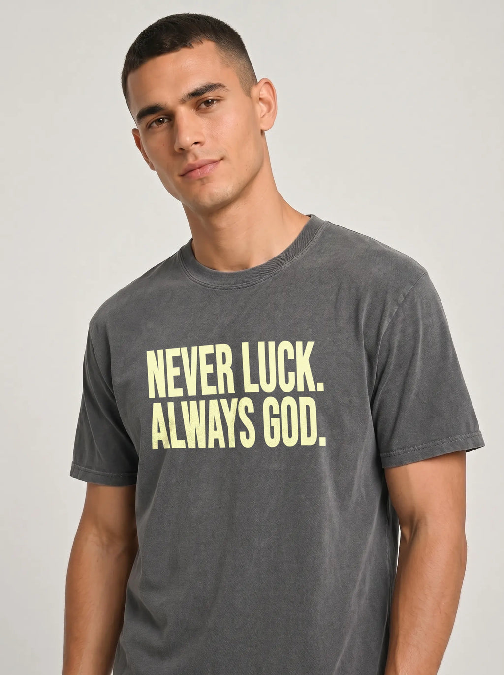 Close-up of a person wearing a faded charcoal T-shirt reading “Never luck. Always God.”