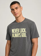 Close-up of a person wearing a faded charcoal T-shirt reading “Never luck. Always God.”