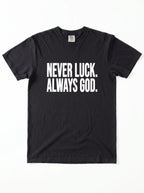 Black T-shirt laid flat with white text reading “Never luck. Always God.”