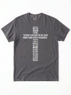 Washed charcoal-gray T-shirt laid flat with white text quoting 2 Corinthians 12:9: “My grace is sufficient for you, for my power is made perfect in weakness.”