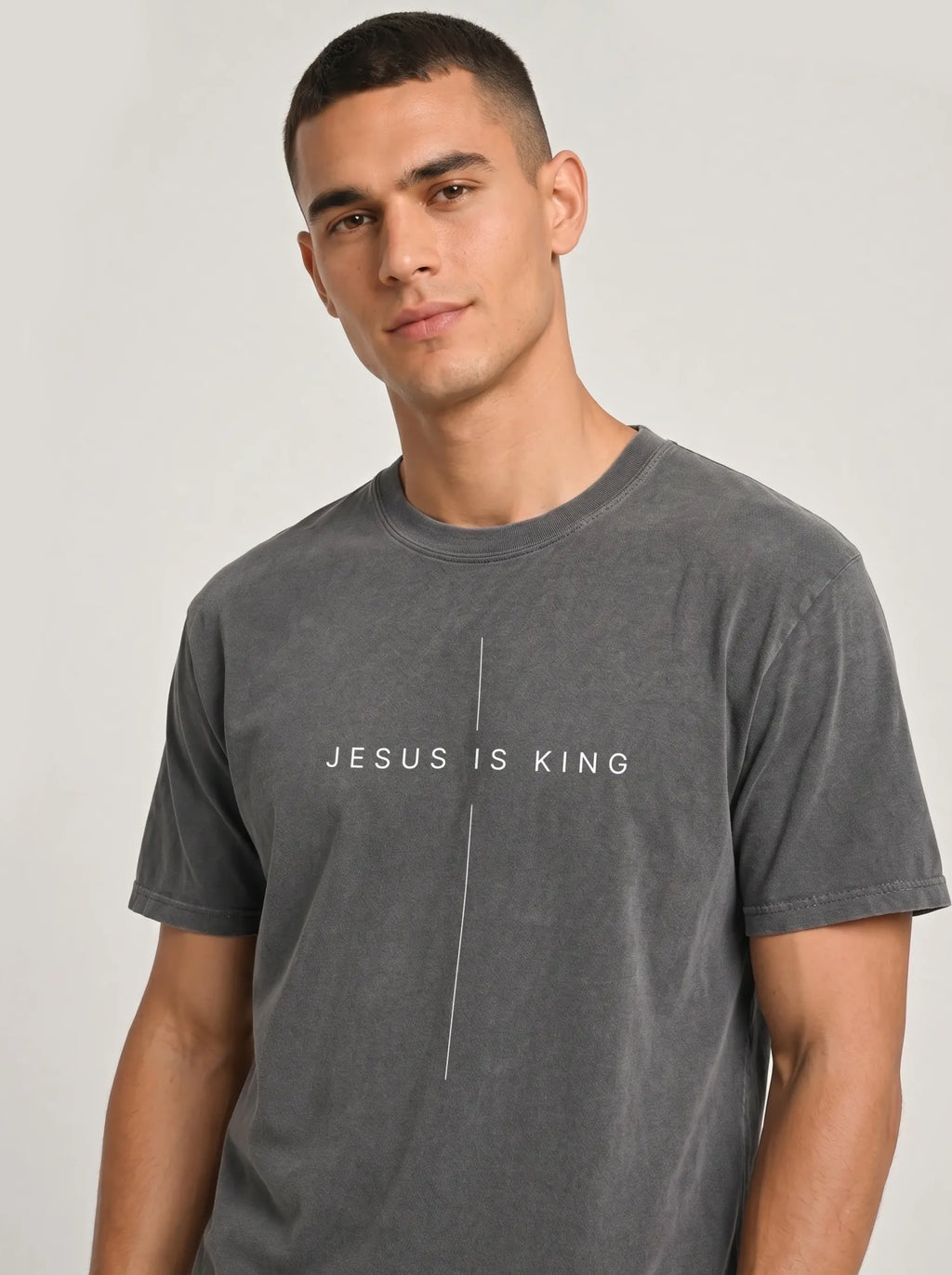 A man wearing a dark gray washed t-shirt with the text 'JESUS IS KING' printed in white across the chest, separated by a vertical line.