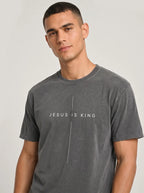 A man wearing a dark gray washed t-shirt with the text 'JESUS IS KING' printed in white across the chest, separated by a vertical line.