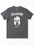 A dark gray crewneck t-shirt with a white graphic print featuring the word 'SALVATION' above a Spartan helmet illustration and the bible verse 'EPHESIANS 6:17'.