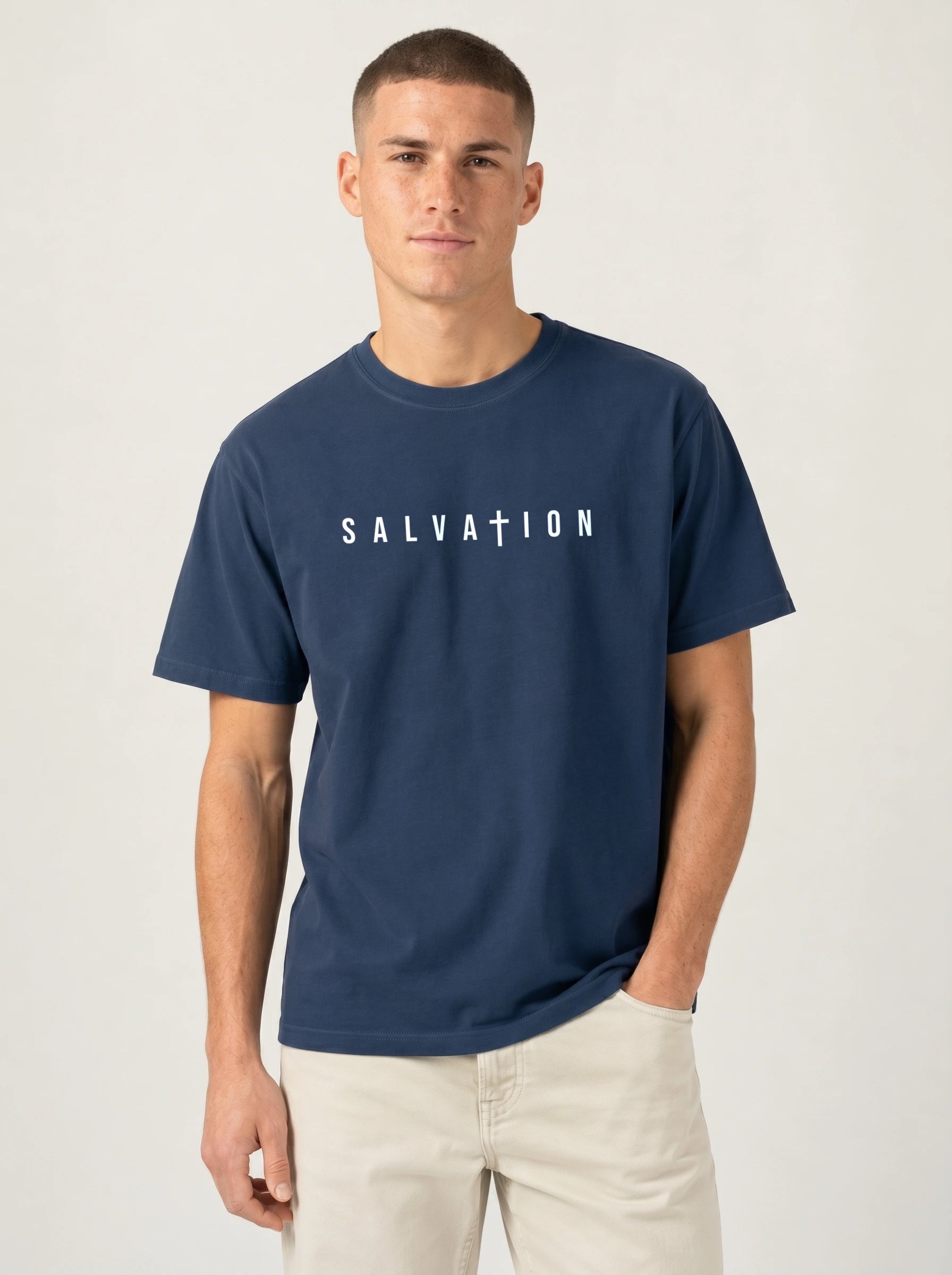 A man wearing a navy blue t-shirt with the word 'SALVATION' printed in white across the chest, paired with light beige pants, against a plain light gray background.