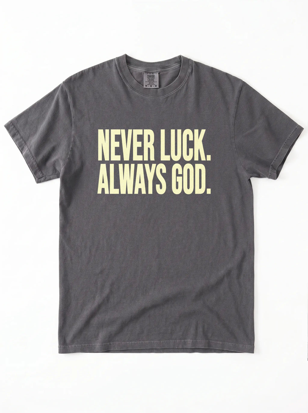 Faded charcoal T-shirt laid flat with pale yellow text reading “Never luck. Always God.”