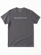 Faded charcoal T-shirt laid flat with the text “Walking by faith” and a small cross beneath it.