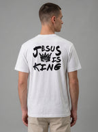 A man viewed from the back wearing a white t-shirt with a black graphic print that reads 'JESUS IS KING' with a crown illustration, paired with khaki pants against a solid gray studio background.