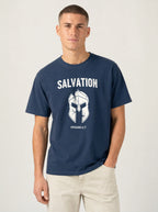 A man wearing a navy blue t-shirt with a white graphic print of a helmet and the word 'SALVATION' on the front, paired with light beige pants, against a plain light gray background.