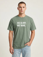 Man wearing a moss green Comfort Colors garment-dyed t-shirt printed with 'His Glory. Not Mine.' Christian faith quote
