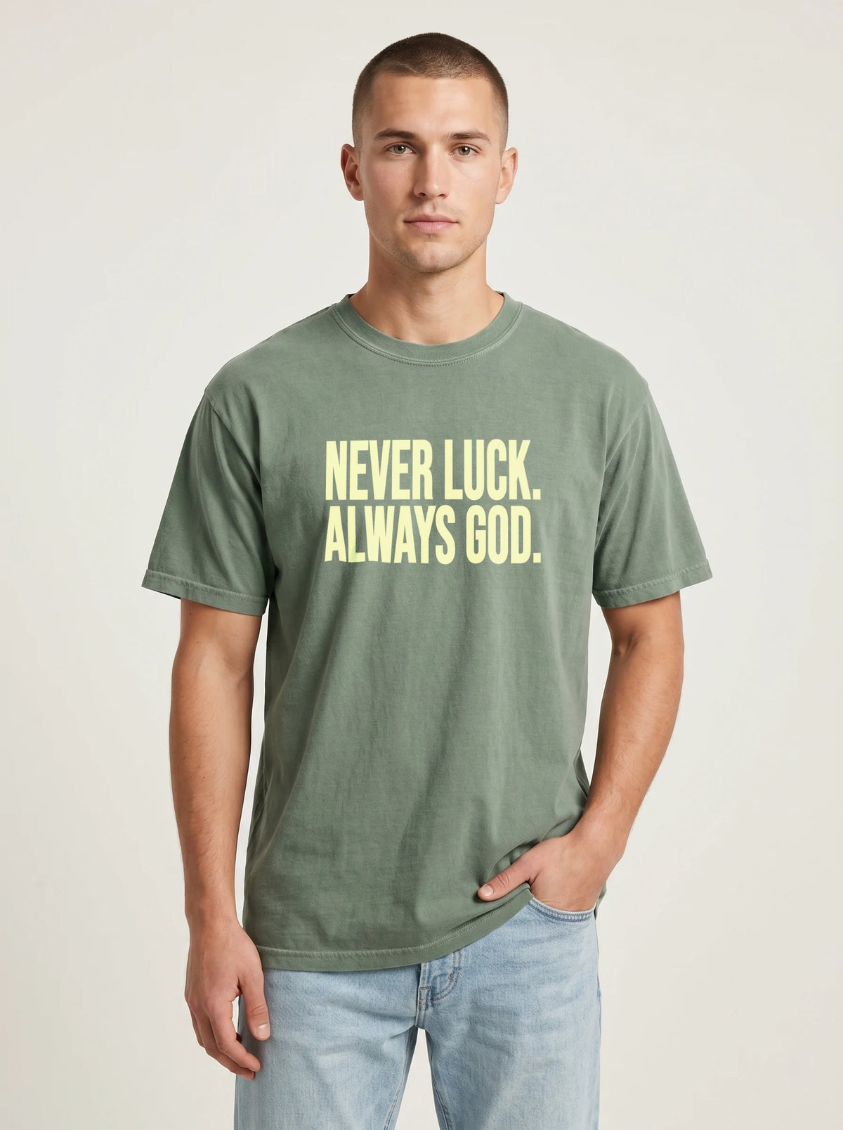 Person wearing a faded green T-shirt reading “Never luck. Always God.” in pale yellow lettering.