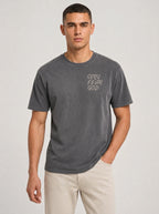 A man wearing a dark gray washed t-shirt with 'ONLY FEAR GOD'' printed in white on the left chest, paired with beige pants, against a light gray studio background.