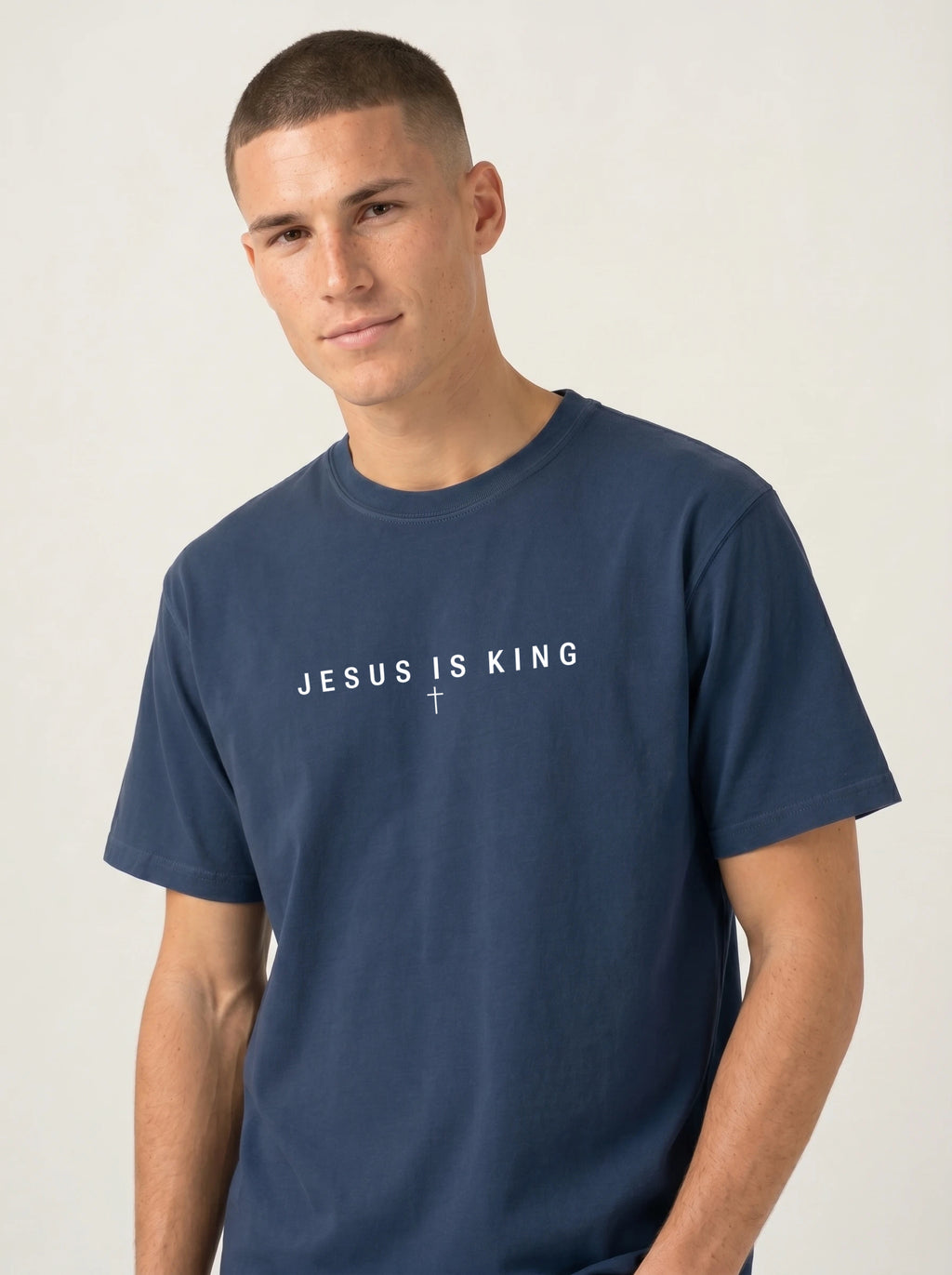 A man wearing a navy blue crewneck t-shirt with the text 'JESUS SAVES' and a cross printed in white across the chest, photographed against a light gray studio background.