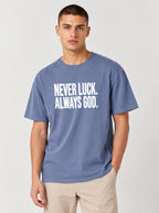 Person wearing a faded blue T-shirt with white text reading “Never luck. Always God.”