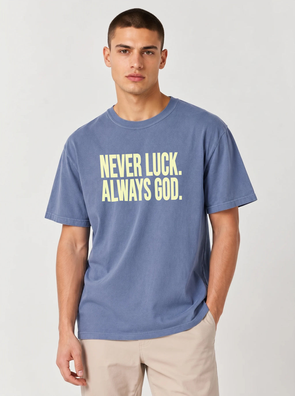Person wearing a faded blue T-shirt reading “Never luck. Always God.” in pale yellow lettering.