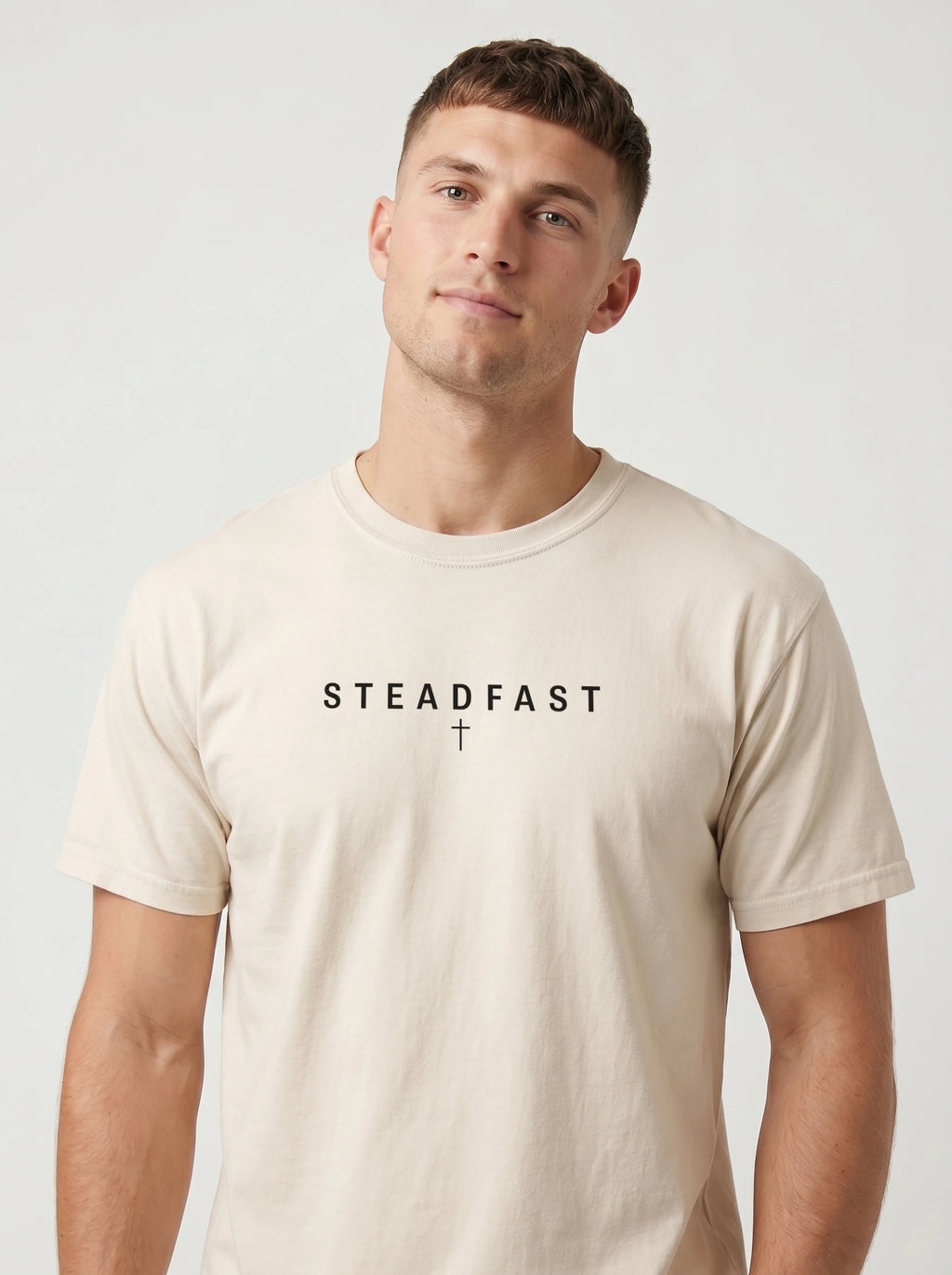 Person wearing a cream T-shirt with the text “Steadfast” and a small cross beneath it.
