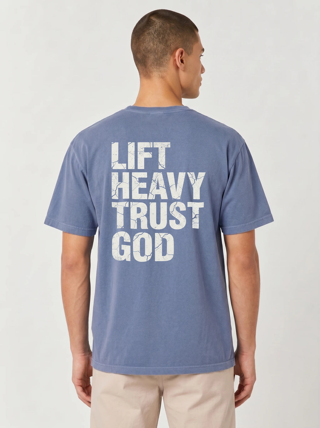 A man viewed from the back wearing a heathered blue t-shirt with distressed white text that reads 'LIFT HEAVY TRUST GOD'.