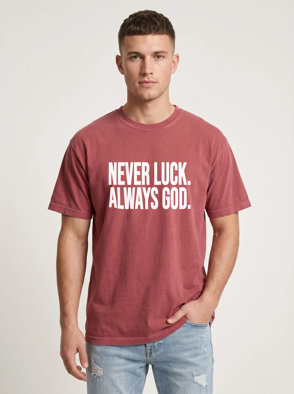 Person wearing a faded red T-shirt with white text reading “Never luck. Always God.”