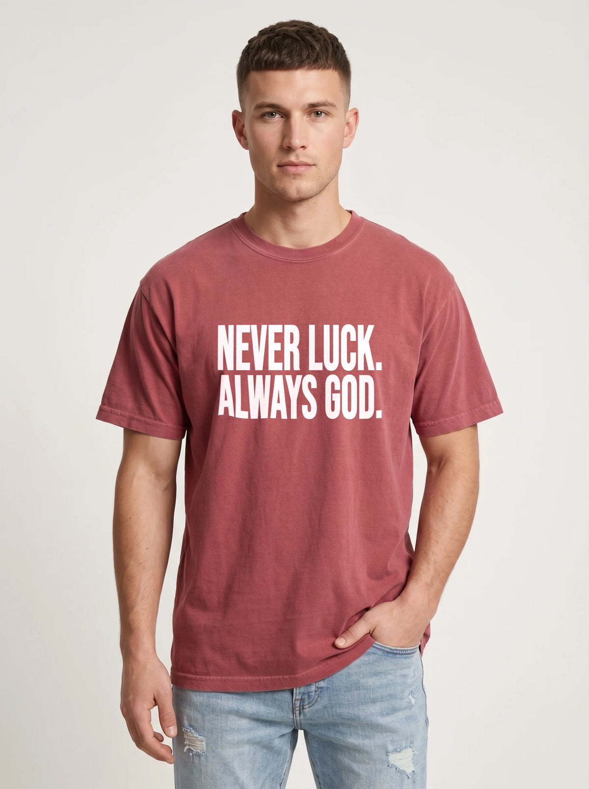 Person wearing a faded red T-shirt with white text reading “Never luck. Always God.”