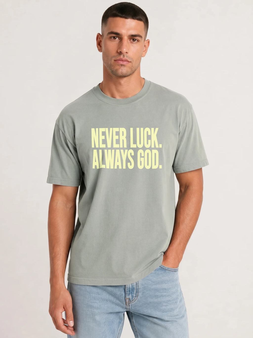 Person wearing a light sage green T-shirt reading “Never luck. Always God.” in pale yellow lettering.