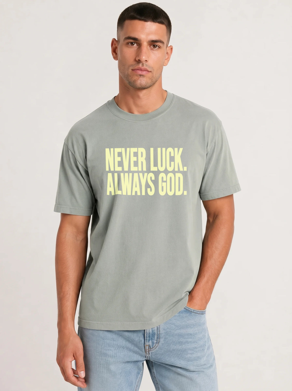 Person wearing a light sage green T-shirt reading “Never luck. Always God.” in pale yellow lettering.