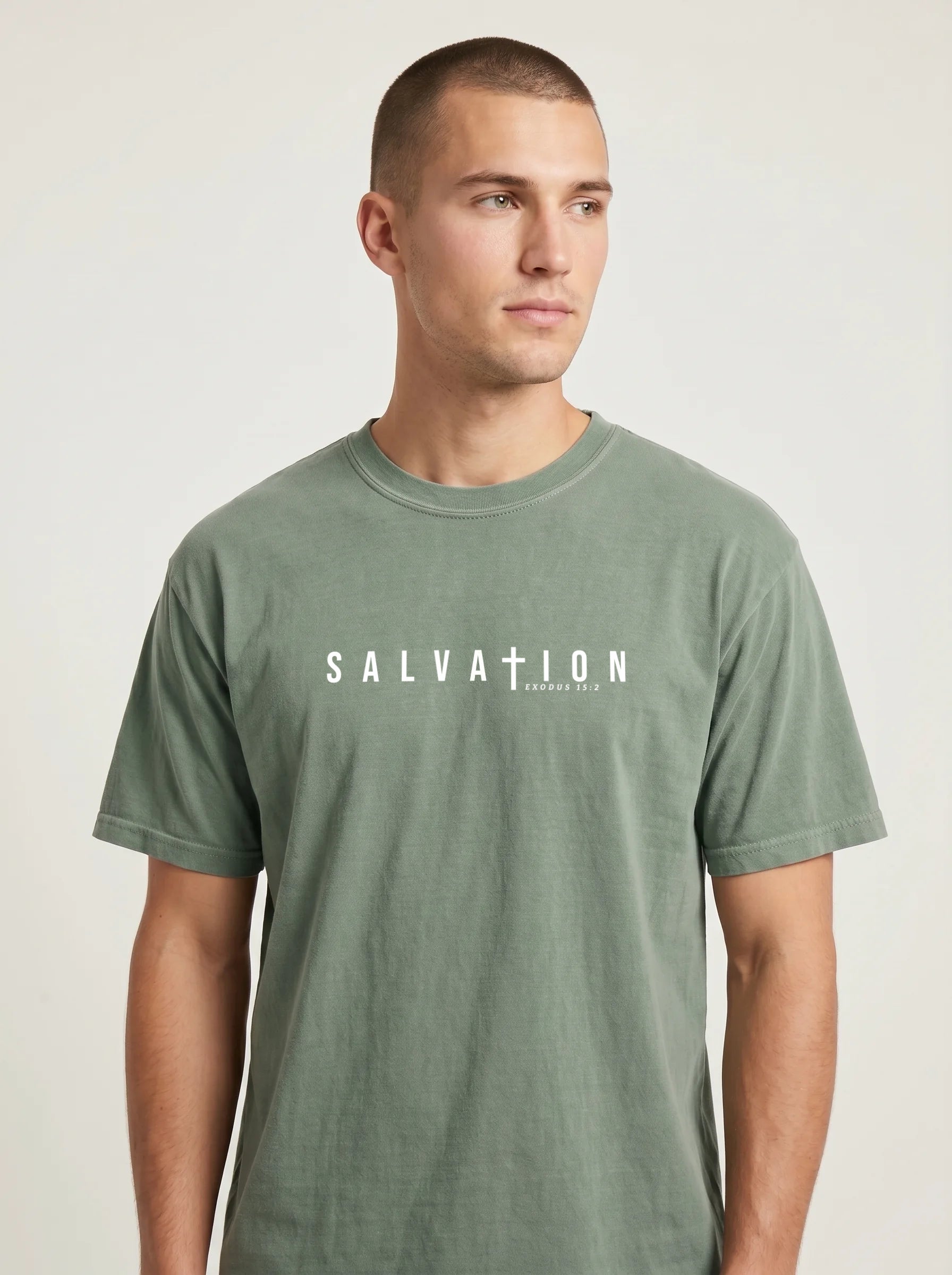 A man wearing a muted sage green t-shirt with 'SALVATION' printed in white across the chest, photographed against a neutral light gray background.