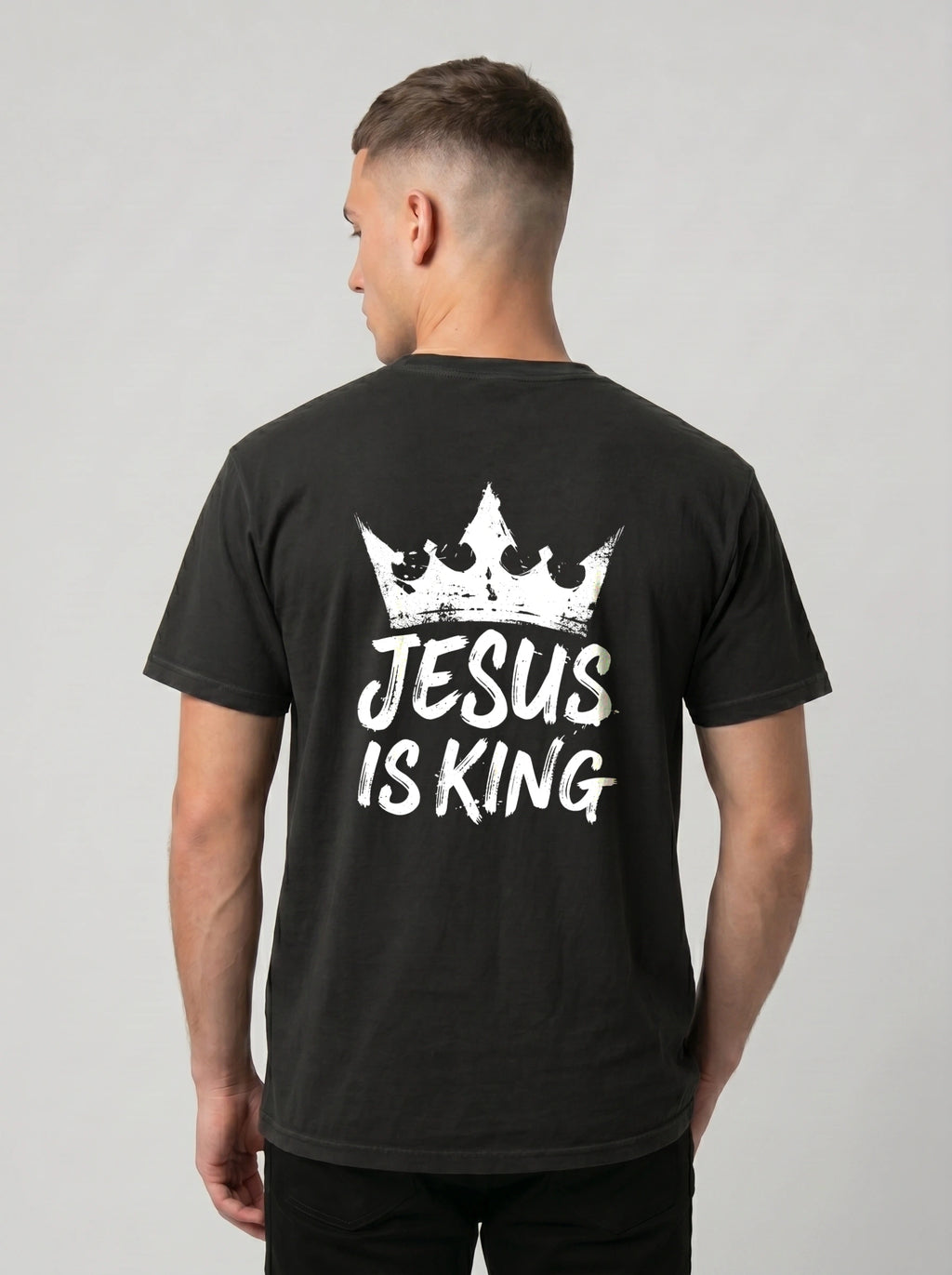 A man viewed from the back wearing a black t-shirt with a white graphic of a crown and the text 'JESUS IS KING'.